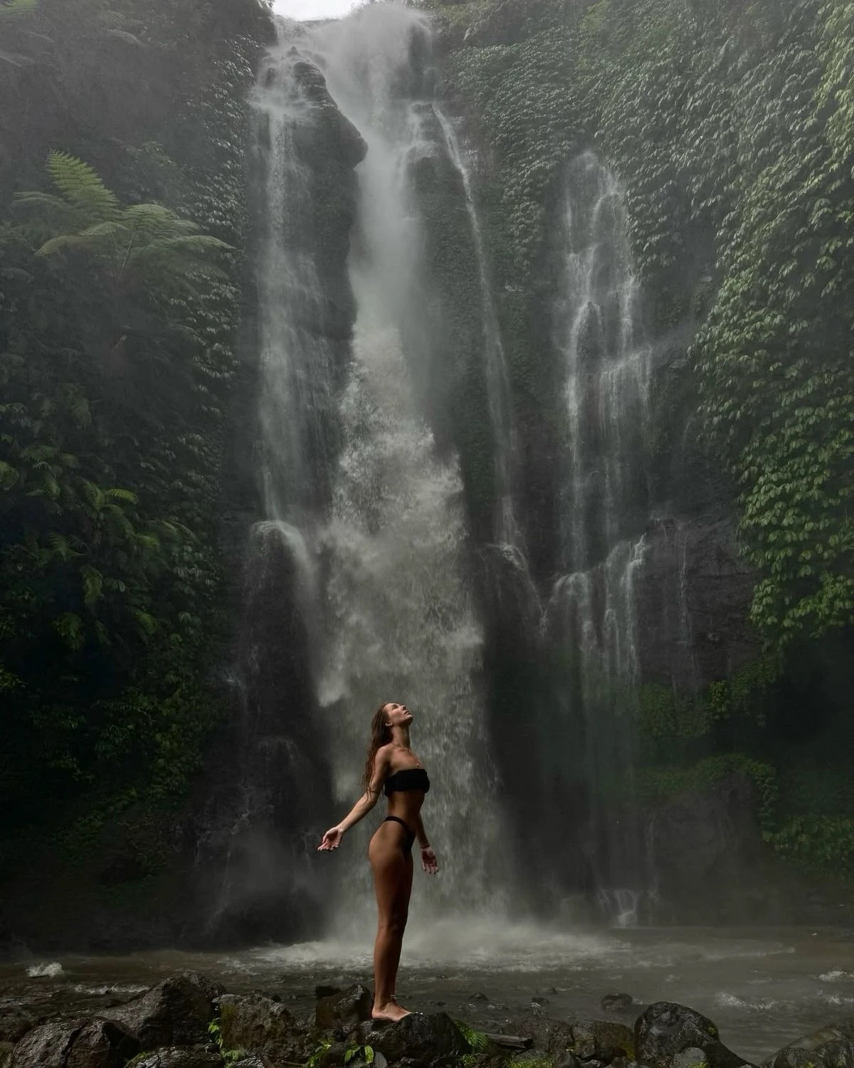A girl standing beneath a jungle waterfall in Bali